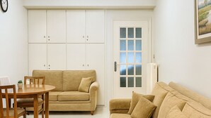 Una sala de estar con un sofá, una mesa de comedor con sillas, un reloj y una puerta con paneles de vidrio esmerilado.