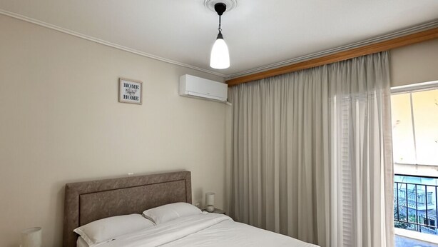 Habitación de hotel con cama, mesita de noche, lámpara, equipo de aire acondicionado y vistas al exterior.