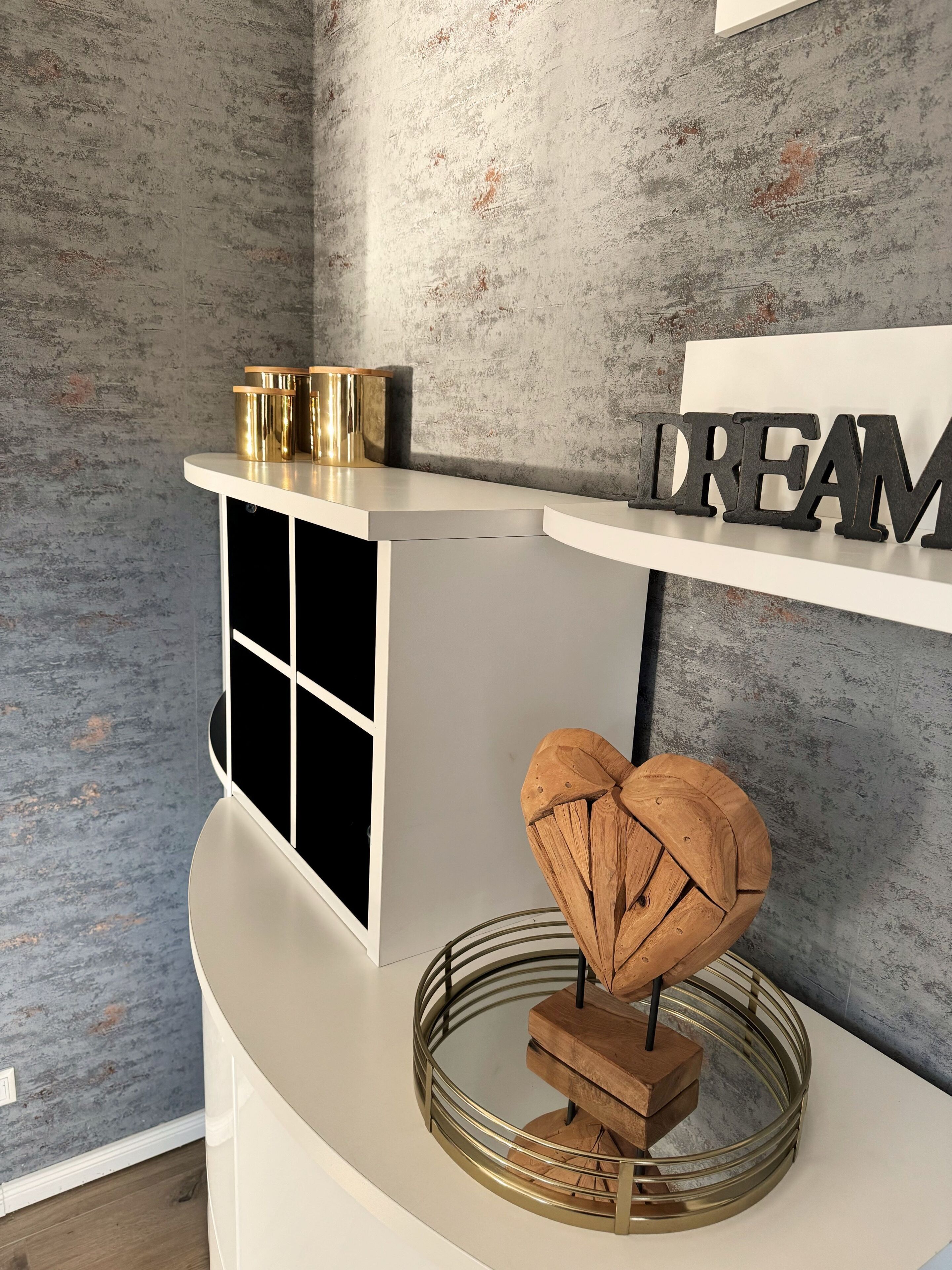 Un interior moderno con una consola blanca, un corazón decorativo sobre un pedestal de vidrio y un estante de pared con la palabra 'DREAMS'.