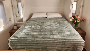 A bed with a textured blanket, a small plant on a shelf above, and a vase with flowers on the right. - Cozy 1-bedroom recreational vehicle in fabulous Las Vegas with AC (Las Vegas)