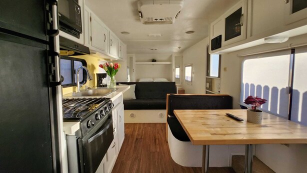 A compact RV kitchen with a stove, sink, and a dining area with a table and chairs. - Cozy 1-bedroom recreational vehicle in fabulous Las Vegas with AC (Las Vegas)