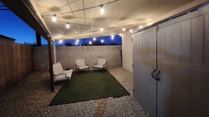 An outdoor patio area with a concrete ceiling, a green artificial turf, three white chairs, and a metal gate. - Cozy 1-bedroom recreational vehicle in fabulous Las Vegas with AC (Las Vegas)