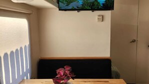 A room with a TV displaying a tropical landscape, a wooden table with a potted plant, and a remote control. - Cozy 1-bedroom recreational vehicle in fabulous Las Vegas with AC (Las Vegas)