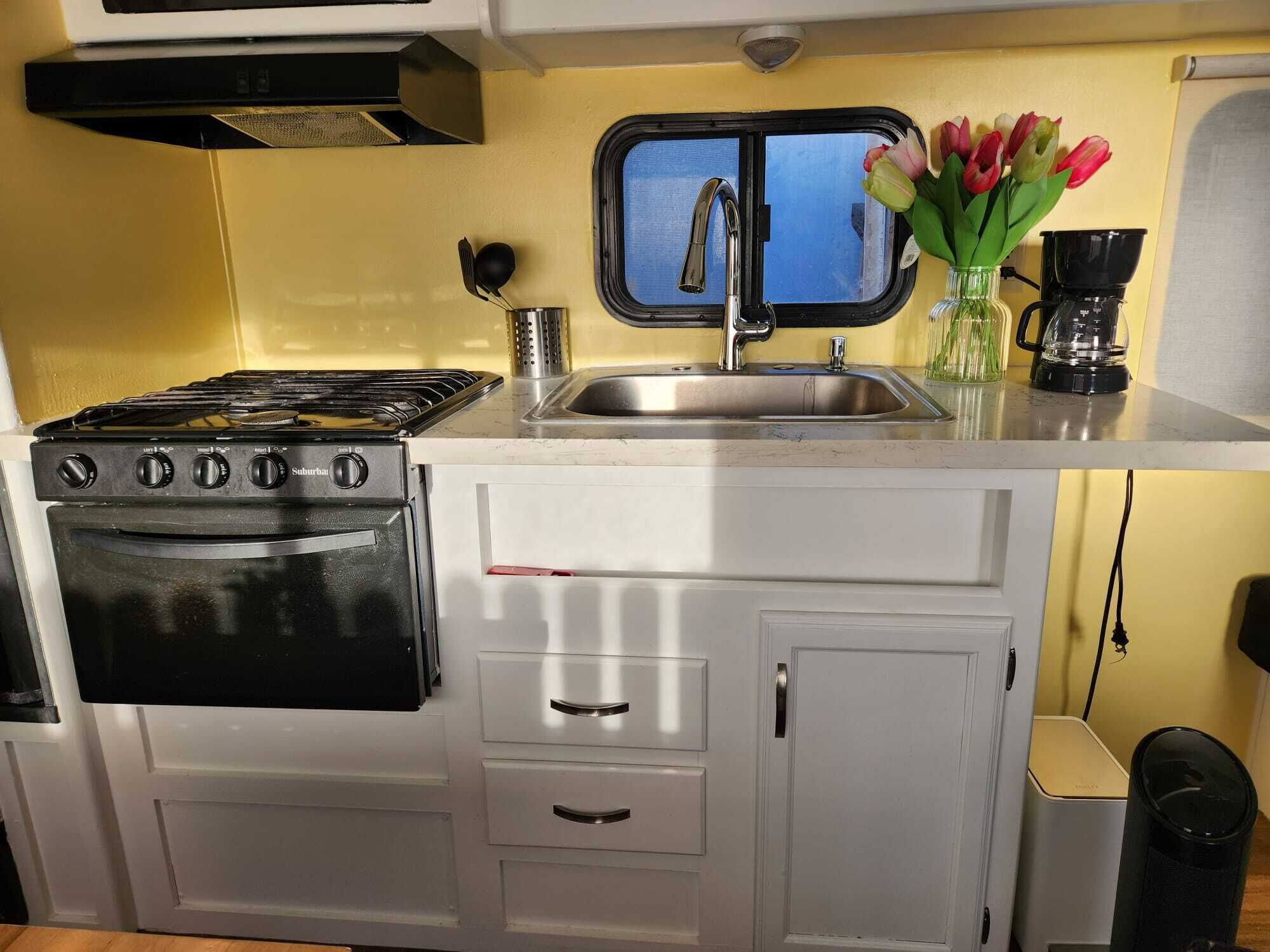 Une cuisine de taille réduite, équipée d’une cuisinière, d’un four, d’un évier et d’une fenêtre située au-dessus de l’évier.