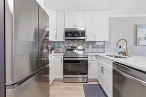 Une cuisine moderne dotée d’appareils électroménagers en acier inoxydable, de meubles blancs et d’un revêtement mural décoratif.