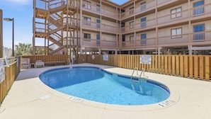 En byggnad med flera våningar, en swimmingpool, ett trädäck och ett badvakts torn.