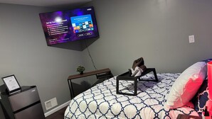 Una camera da letto con un letto, una TV a parete, un tavolino e un frigorifero.