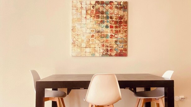 Un comedor con una mesa de madera y dos sillas, una obra de arte abstracta colgada en la pared, y una pared lisa.