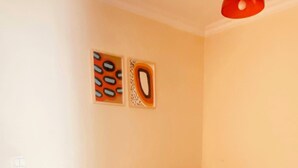 Una habitación pequeña con una cama individual, suelo de madera, colcha amarilla estampada y dos obras de arte en la pared.
