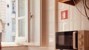 Una cocina con microondas, lavadora y ventana con vistas a edificios.