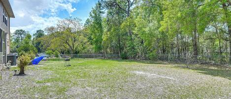 A backyard with a lawn, a tree, and a fence.
