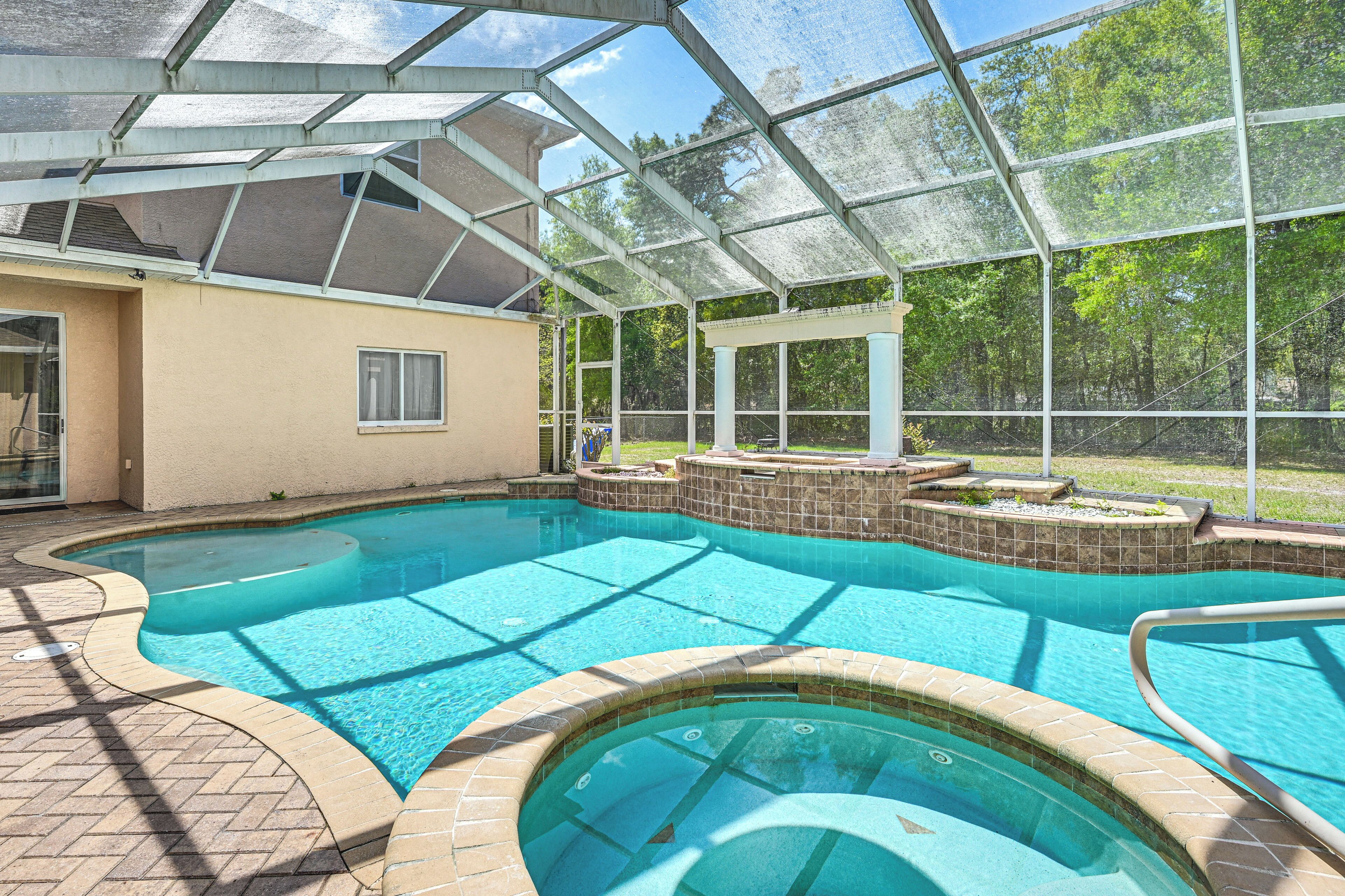 A swimming pool with a glass enclosure, surrounded by a brick deck and a covered patio area.