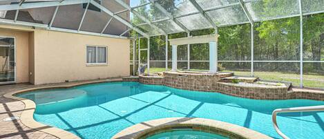 A swimming pool with a glass enclosure, surrounded by a brick deck and a covered patio area.