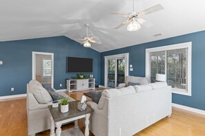 A living room with a sofa, a coffee table, a TV, ceiling fans, and a window with blinds.