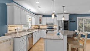 A modern kitchen with white cabinets, granite countertops, a central island, and pendant lighting. - Sandpiper Hideaway - Easy Beach Access (Indian Beach)