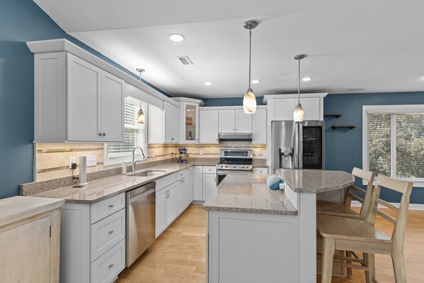A modern kitchen with white cabinets, granite countertops, a central island, and pendant lighting.