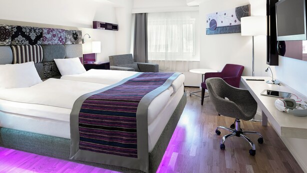 Quarto de hotel moderno com cama, escrivaninha, cadeira e obras de arte.