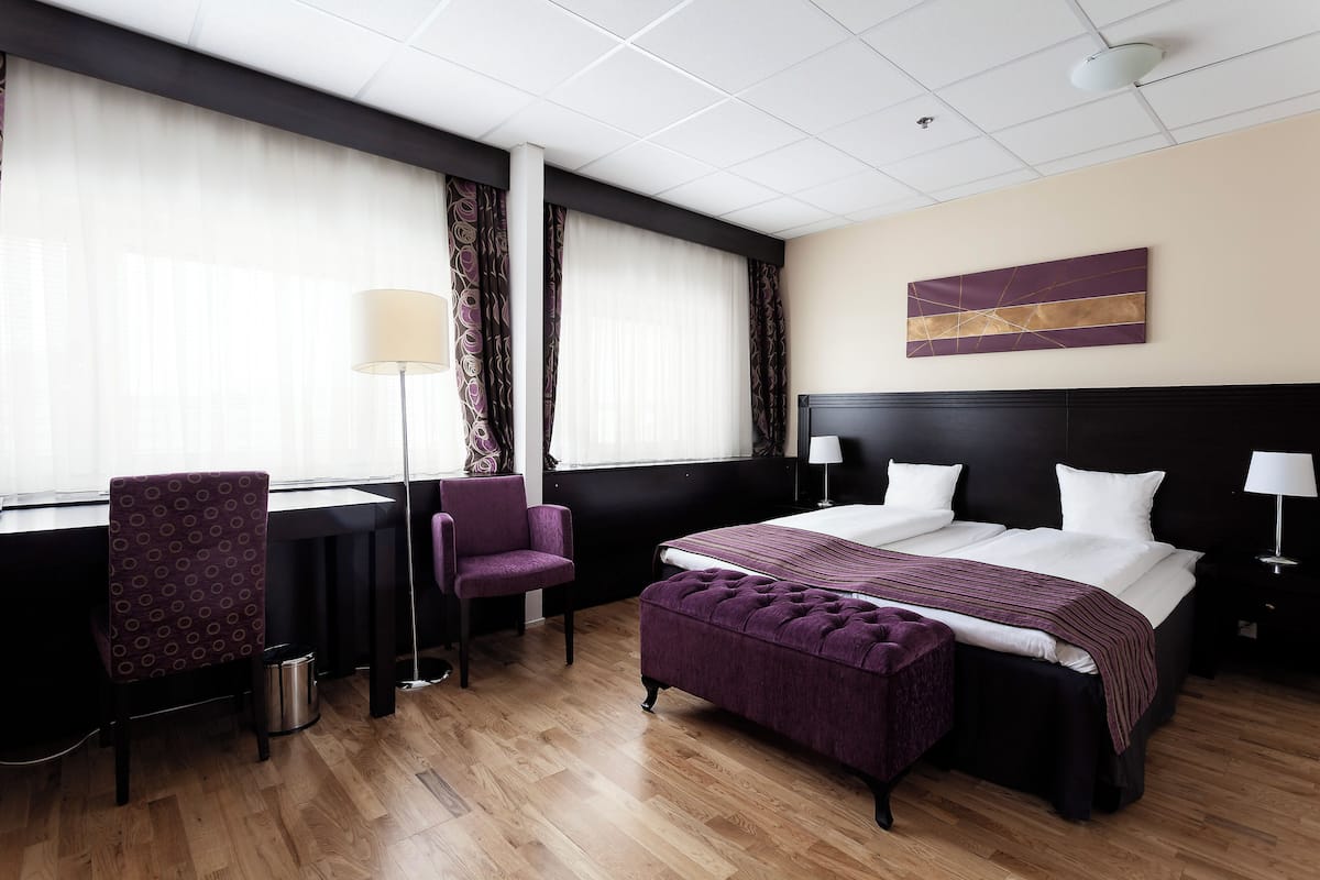 A hotel room with a large bed, a desk, a chair, and a window with curtains.