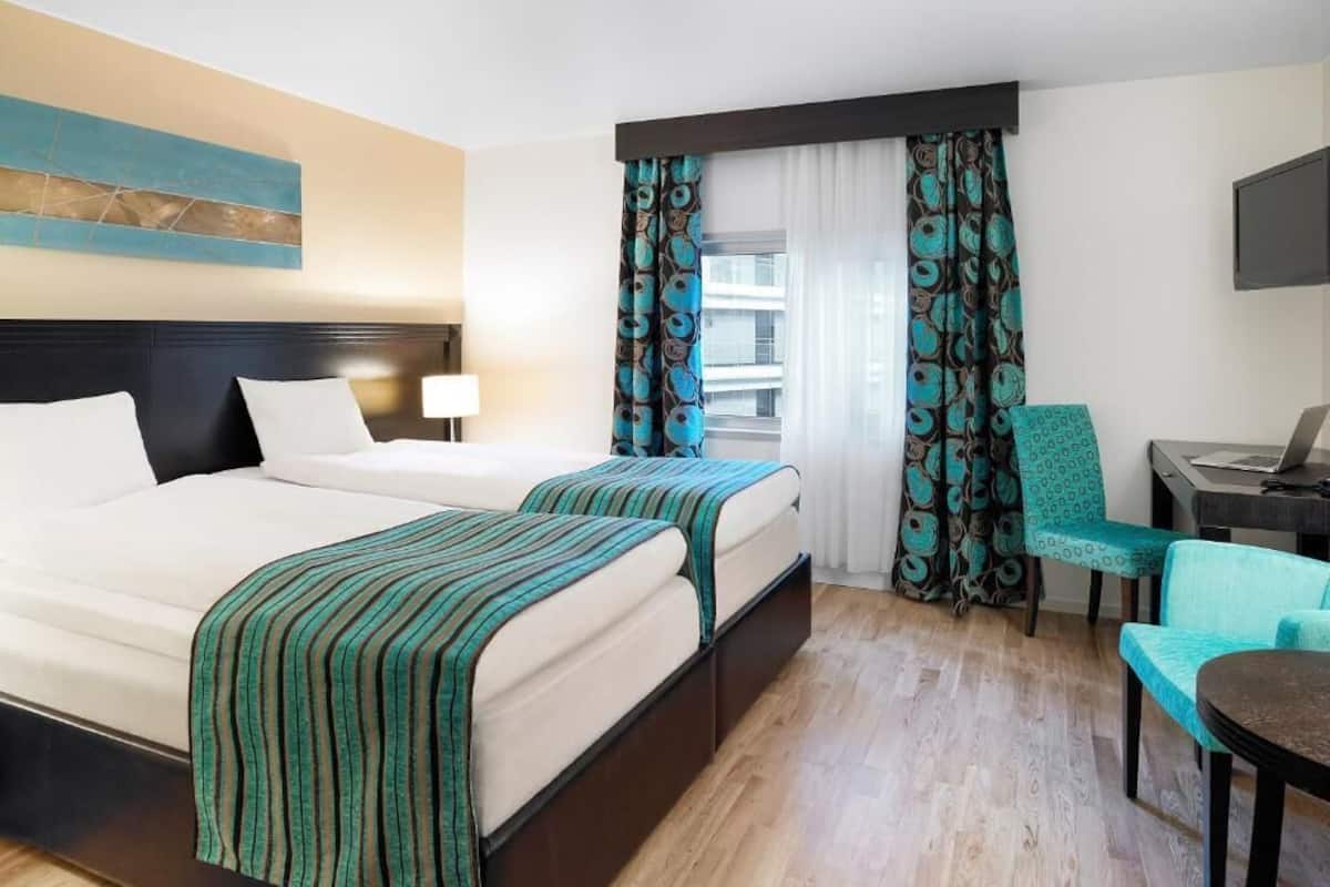 A hotel room with two beds, a desk with a laptop, a chair, and a TV.