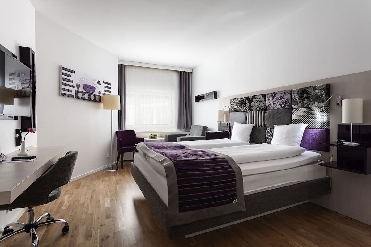A modern hotel room with a bed, desk, chair, and a window with curtains.