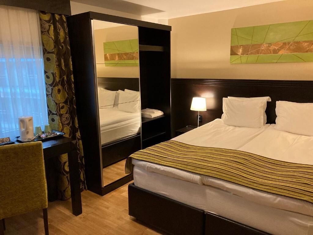 A hotel room with a bed, bedside table, lamp, chair, and a mirror.