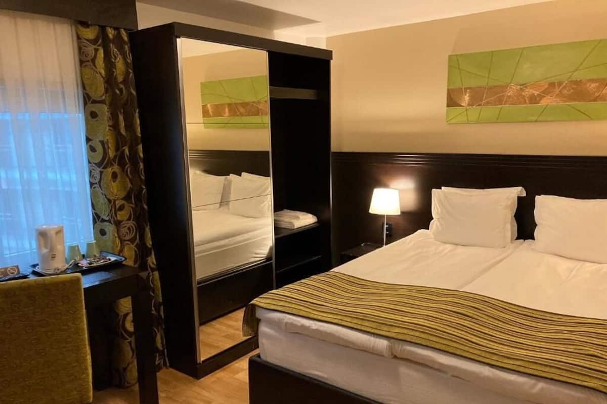 A hotel room with a bed, bedside table, lamp, chair, and a mirror.