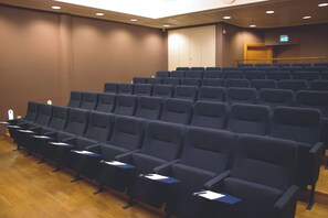 A conference room with rows of chairs, a podium, and a projection screen. - Hoom Park (Solna)