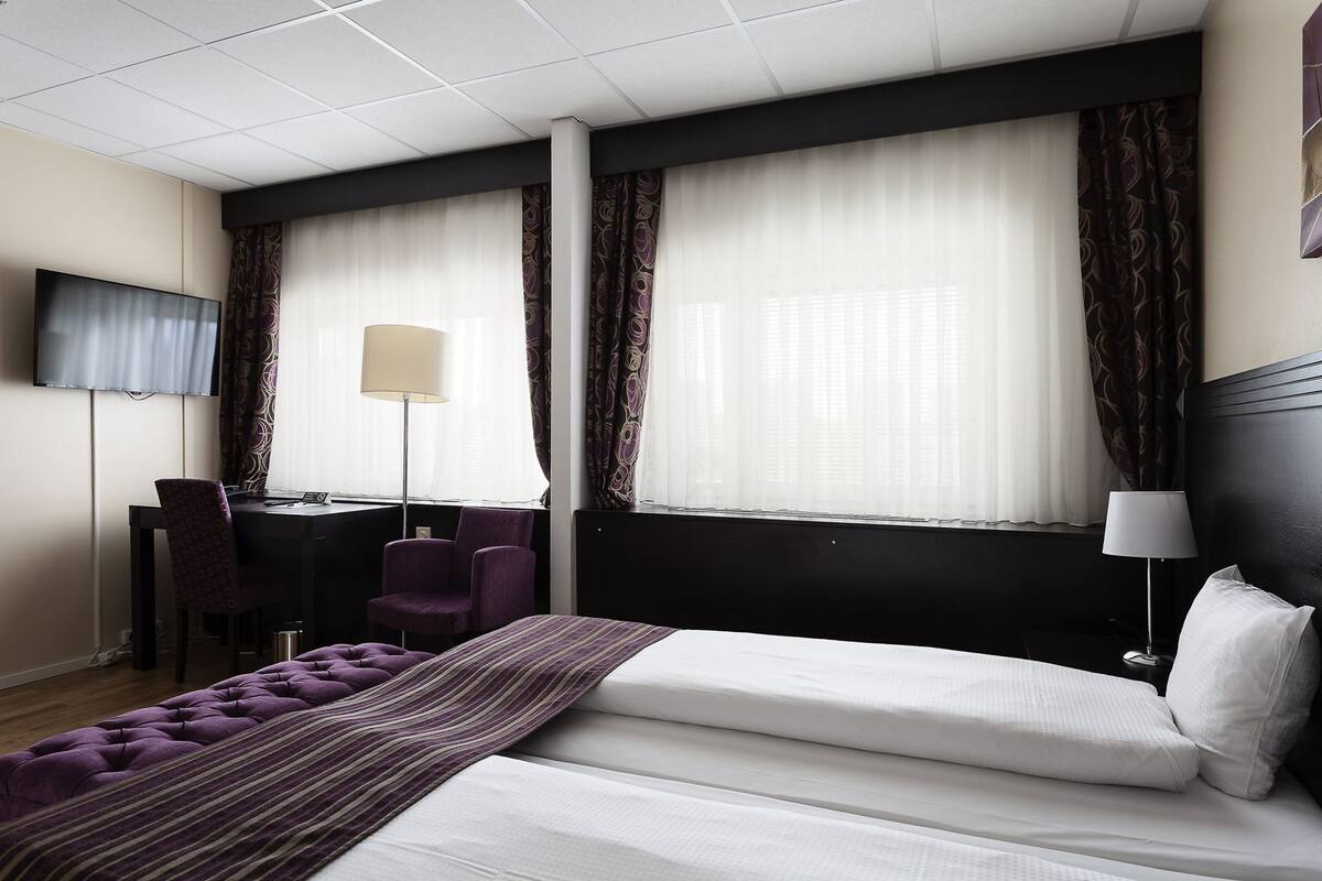 A hotel room with a bed, a desk, a chair, a TV, and curtains.