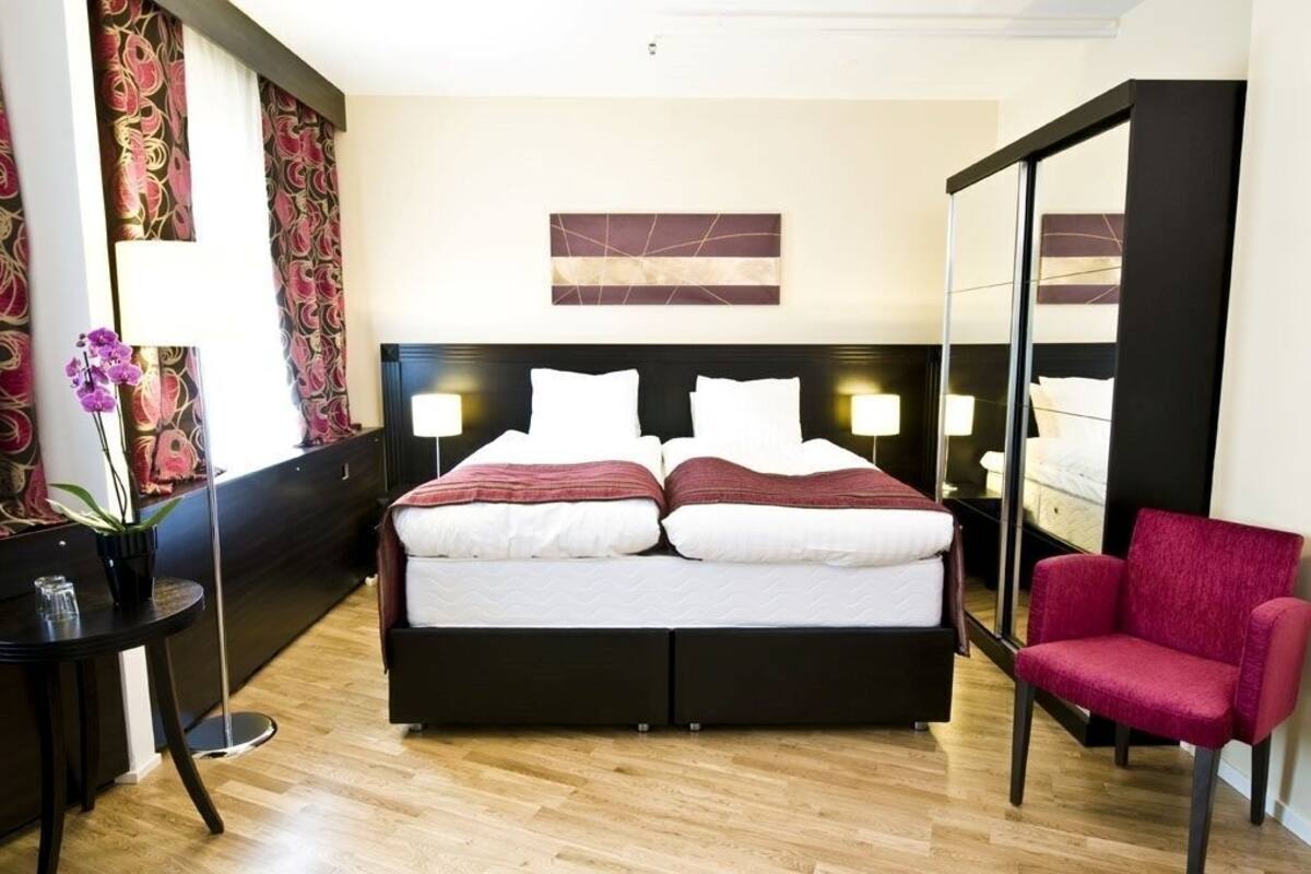 A hotel room with a bed, bedside lamps, a chair, a potted plant, and a mirror.