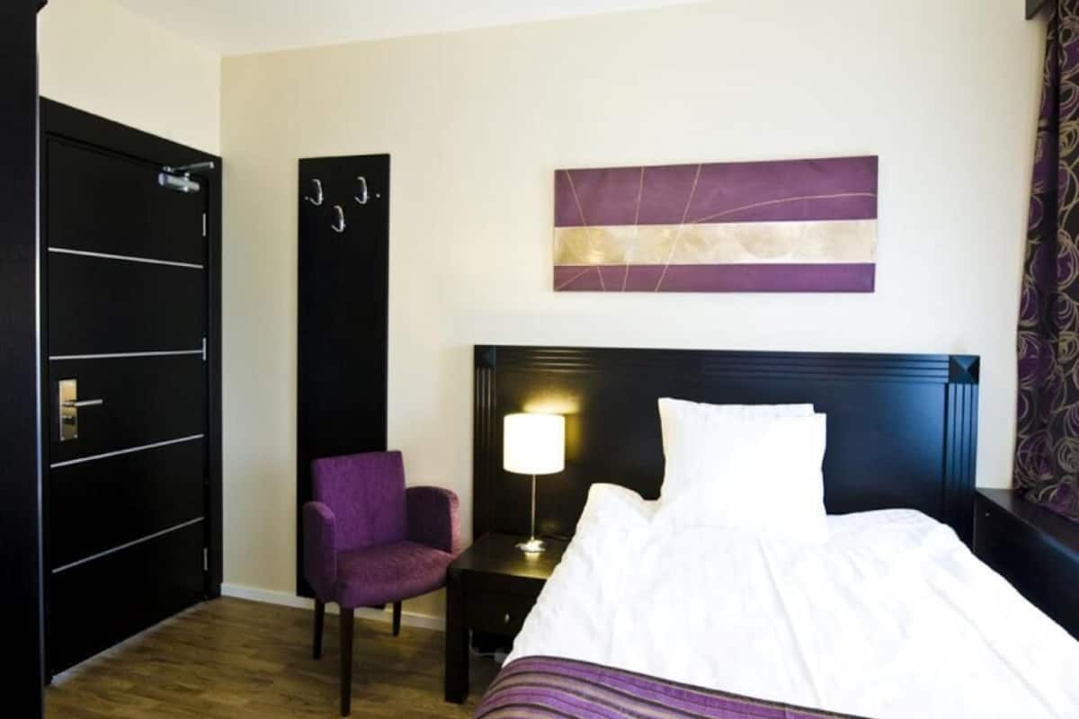 A hotel room with a bed, a nightstand, a chair, a wall-mounted artwork, and a door.
