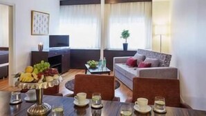 Una habitación de hotel moderna con comedor, sofá, televisor y una planta.