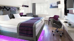 Una habitación de hotel moderna con cama, escritorio, silla y obras de arte.