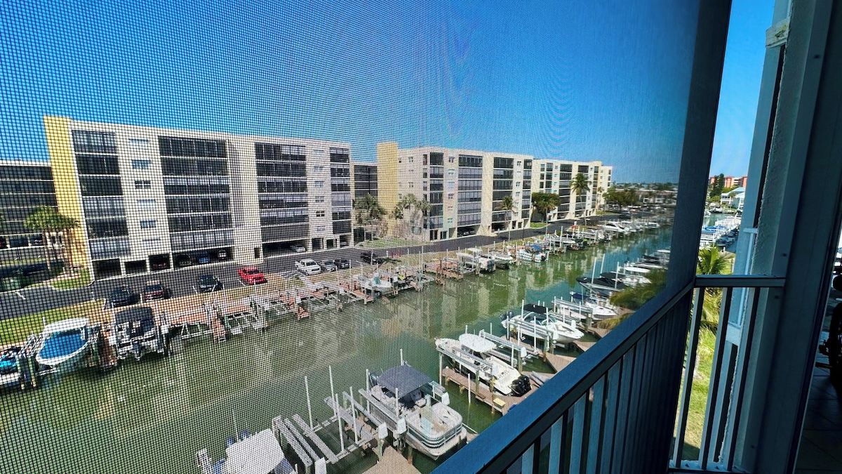 A marina with boats docked, a modern building complex in the background, and a clear sky.