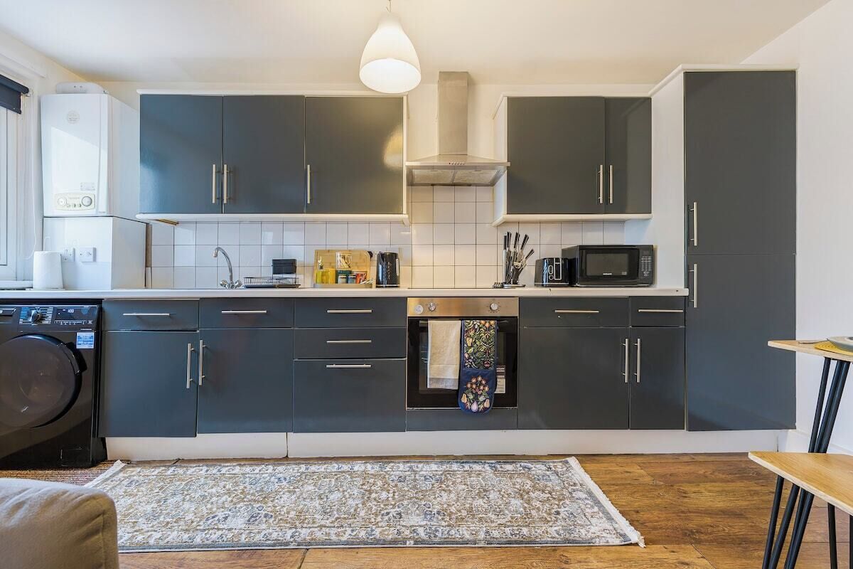 Une cuisine moderne avec des meubles de couleur sombre, un four à micro-ondes et un lave-linge.