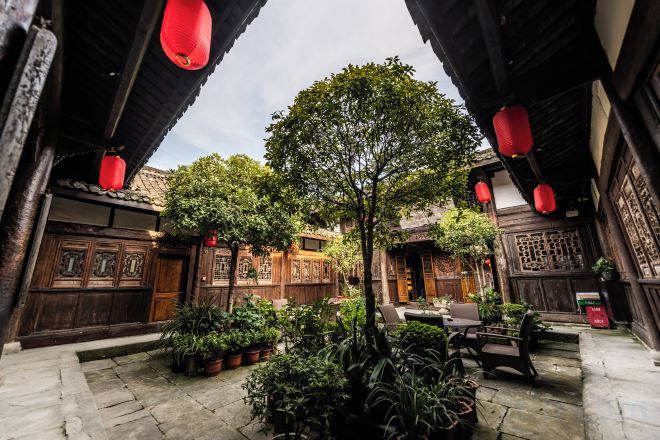 A courtyard with traditional wooden architecture, potted plants, and red lanterns.