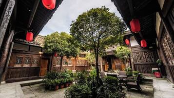 A courtyard with traditional wooden architecture, potted plants, and red lanterns.