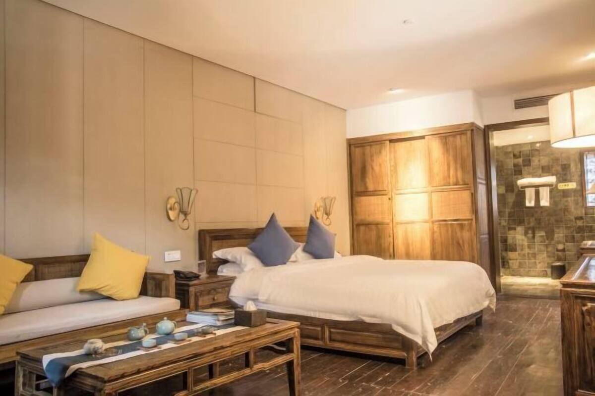 A bedroom with a bed, a sofa, a wooden coffee table, and a wardrobe.