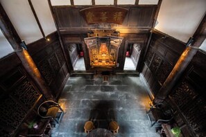 A traditional wooden interior with a central altar, stone flooring, and two chairs. - Langzhong Lijia Quadrangle Inn (Langzhong)
