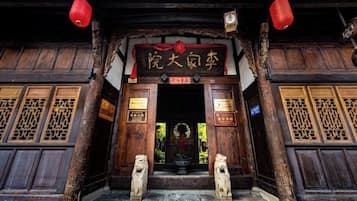 A traditional wooden entrance with a sign, two stone lion statues, and red lanterns.