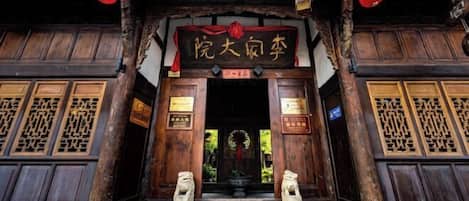 A traditional wooden entrance with a sign, two stone lion statues, and red lanterns.