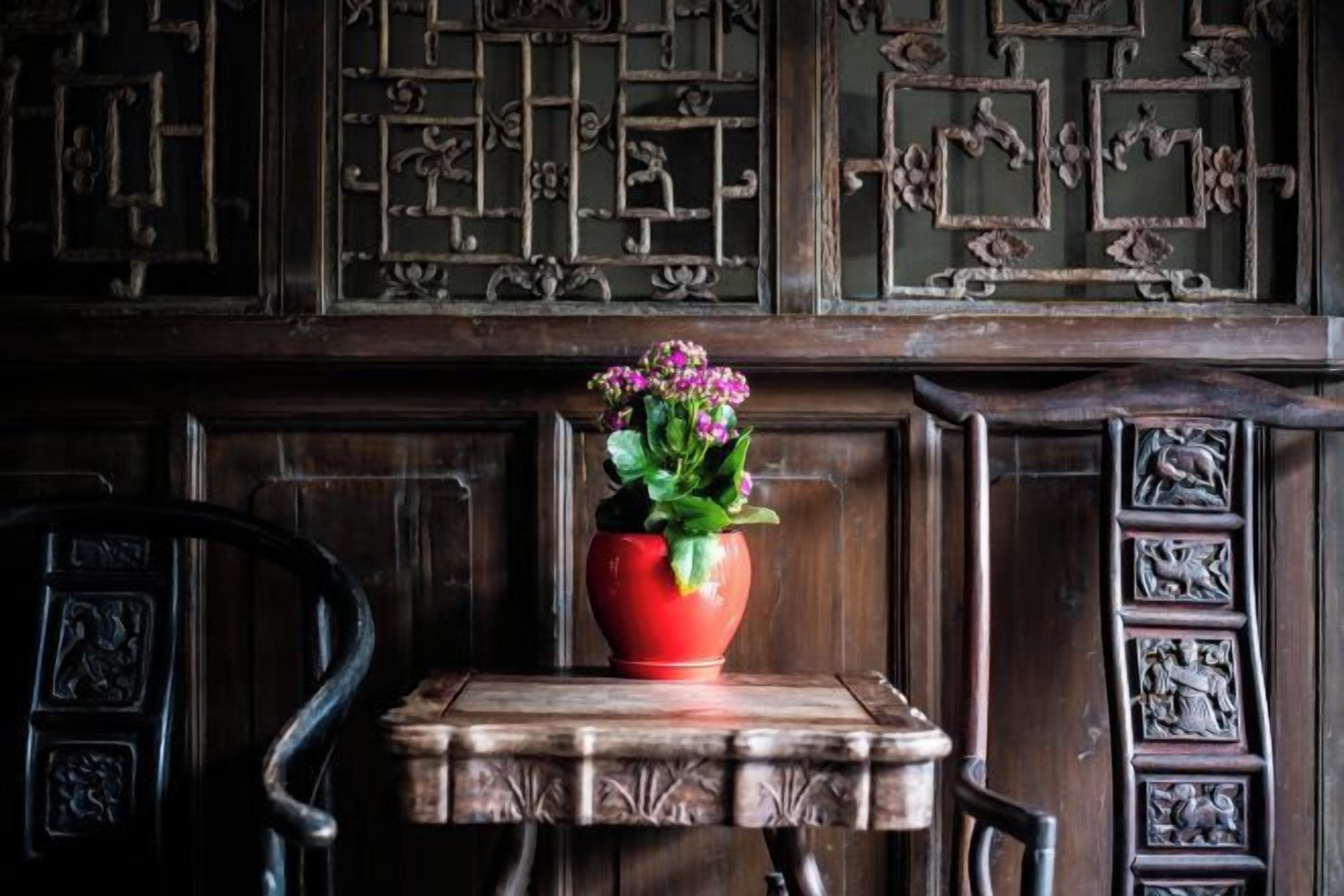 Et træbord med en rød vase med blomster, placeret foran en væg med detaljerede udskæringer.