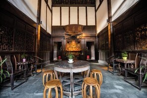 A traditional interior with a round table surrounded by stools, wooden paneling, and a central decorative piece. - Langzhong Lijia Quadrangle Inn (Langzhong)