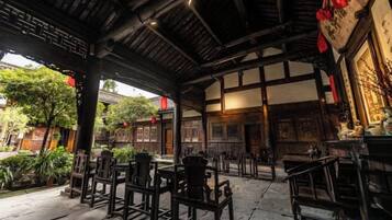 Een traditionele houten constructie met tafels en stoelen, waarschijnlijk een restaurant of theehuis, met uitzicht op de omliggende tuin.