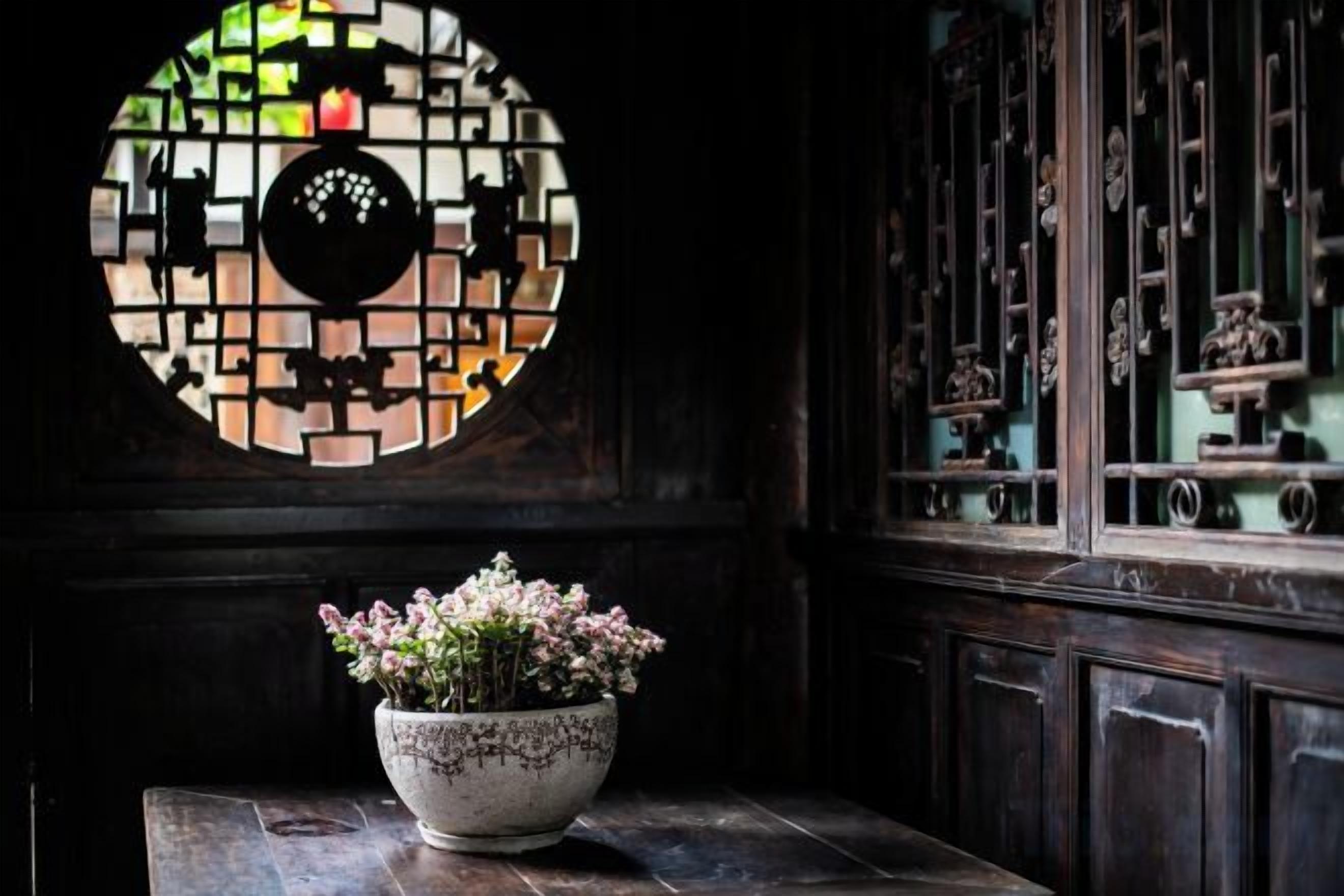 Une pièce dotée d’une fenêtre circulaire en vitrail, d’un meuble en bois aux portes vitrées et d’une plante en pot posée sur une table.