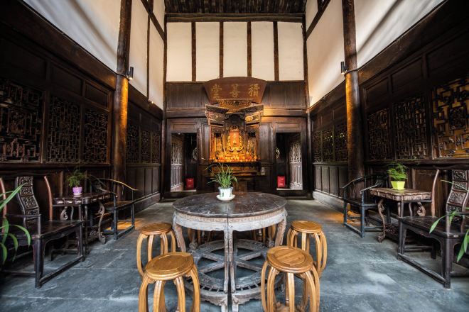 A traditional interior with a round table surrounded by wooden stools, a central decorative element, and patterned walls.