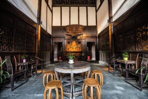 A traditional interior with a round table surrounded by wooden stools, a central decorative element, and patterned walls. - Langzhong Lijia Quadrangle Inn (Langzhong)