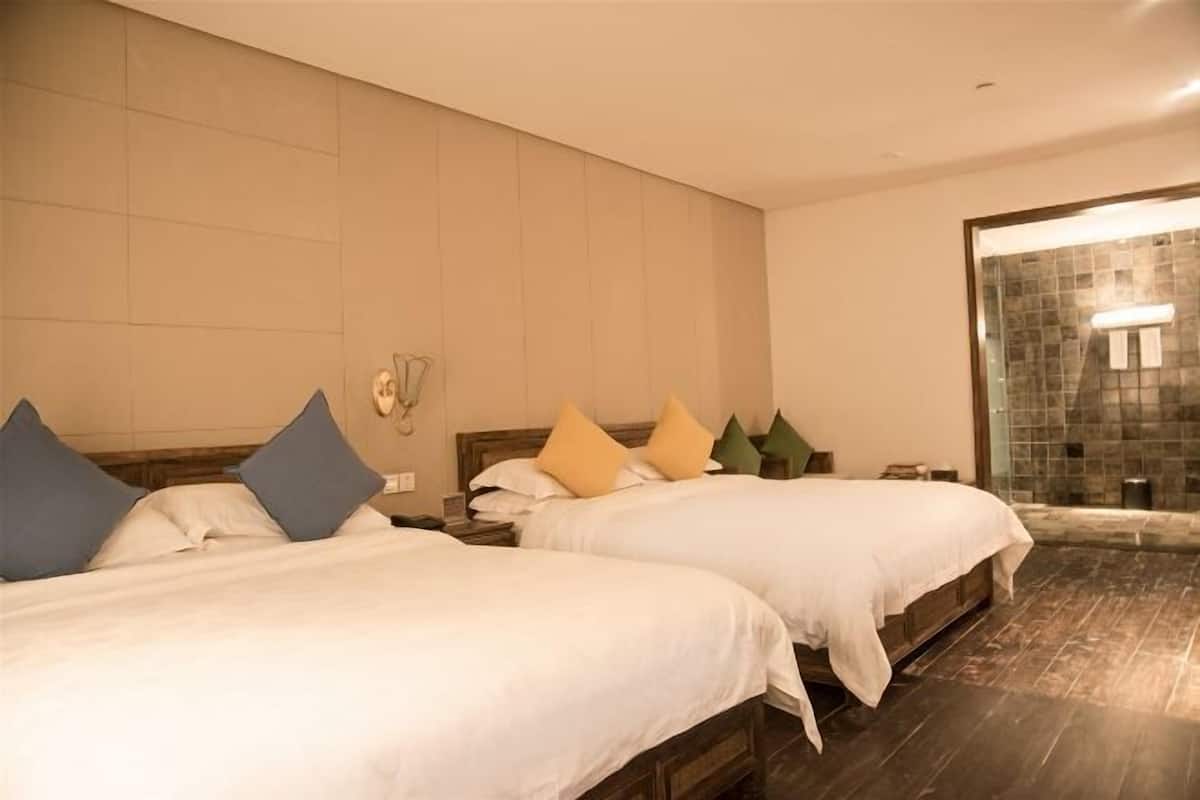 A hotel room with two beds, a bathroom with a stone wall, and a wooden floor.