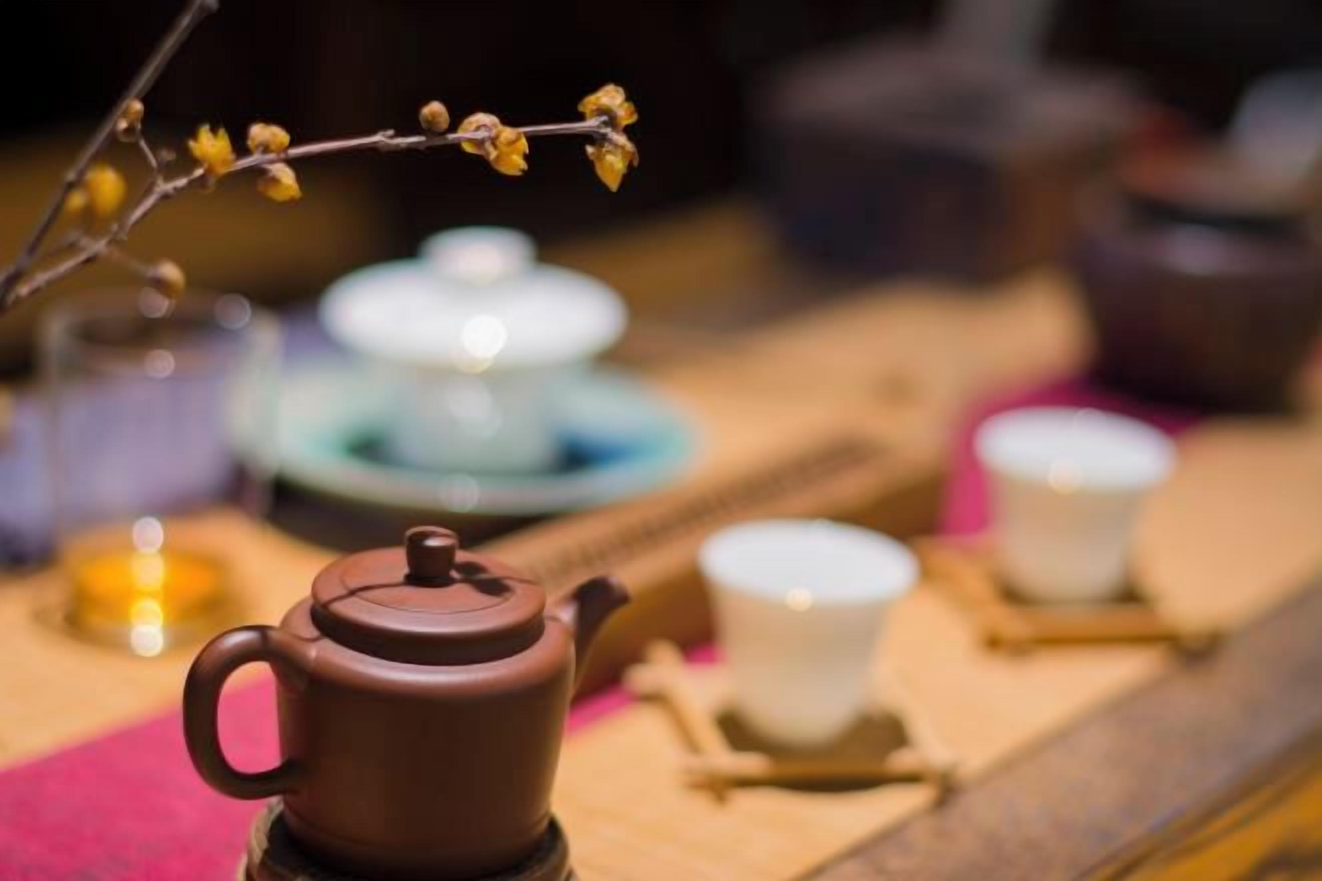 A teapot on a coaster, a cup, and a saucer on a table with a blurred background.