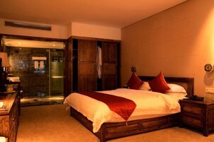 Habitación de hotel con una cama grande, un armario de madera, un escritorio con lámpara y un baño con cabina de ducha de vidrio.