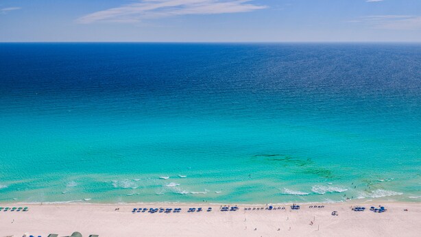 Une plage avec une eau turquoise et limpide, un rivage sablonneux et des parasols.